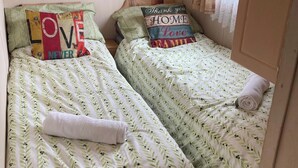 Twee enkele bedden met beddengoed met bladmotieven, kussens met tekst, en een opgerolde handdoek op elk bed.
