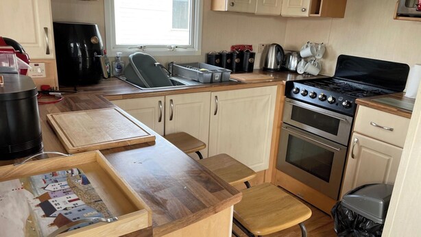 Een kleine keuken met een kookplaat, oven, spoelbak en houten aanrecht.