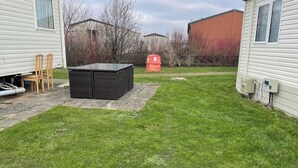 Een gazon met een zwarte buitentafel en stoelen, een rode brievenbus en een functionele doos.