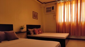 A hotel room with two beds, a nightstand, a potted plant, a framed picture, an air conditioning unit, and a window with curtains. - Fiesta Ballroom Hotel (Legazpi)