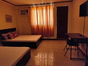 A hotel room with two beds, a desk, a chair, a TV, and a window with curtains.