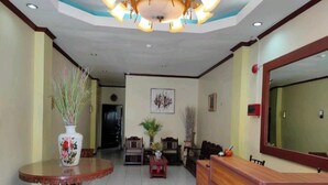 A reception area with a wooden reception desk, a round table with a vase, and a seating area with chairs and a small table. - Fiesta Ballroom Hotel (Legazpi)
