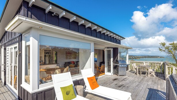 A modern house with a deck, outdoor seating, and a view of the water. - Pacific Views - Waiheke Island (Waiheke Island)