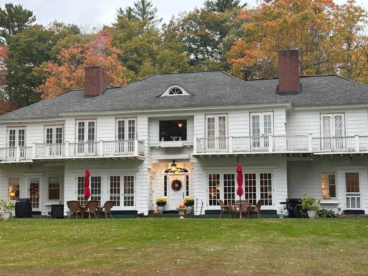 A two-story white building with a balcony, a front door with a wreath, and outdoor seating with umbrellas.