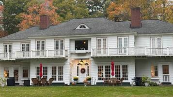 A two-story white building with a balcony, a front door with a wreath, and outdoor seating with umbrellas.