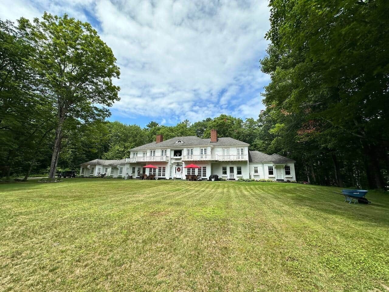 Een groot wit huis met een veranda, omringd door een verzorgd gazon en bomen.