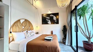 A modern bedroom with a large bed, a wall-mounted painting, and a potted plant by the window. - Palazzo Pappagalo (Canggu)