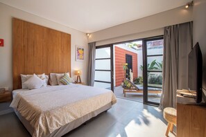 Een moderne slaapkamer met een groot bed, een televisie en een schuifdeur die leidt naar een balkon met een rode bakstenen muur en beplanting.