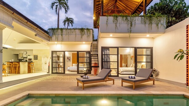 Una casa moderna con piscina, sillas de descanso y un dormitorio visible a través de puertas de vidrio.