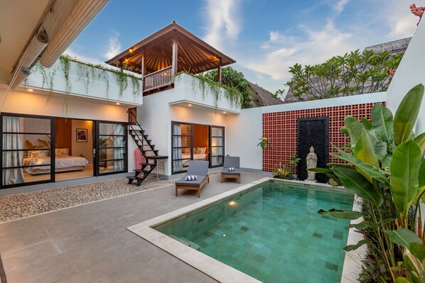 Een moderne villa met een privézwembad, een overdekt terras en een trap naar een slaapkamer.
