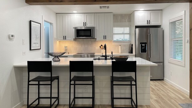 Una cocina moderna con armarios blancos, electrodomésticos de acero inoxidable y techo de madera.