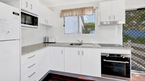 A modern kitchen with white cabinets, a built-in microwave, a dishwasher, and a window with a valance. - Highset one street back from the beach (Woodgate)
