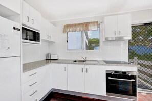 A modern kitchen with white cabinets, a built-in microwave, a dishwasher, and a window with a valance.