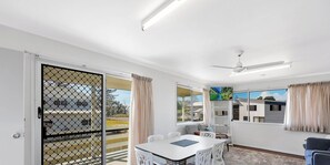 A room with a dining table, chairs, a TV mounted on the wall, and a ceiling fan.