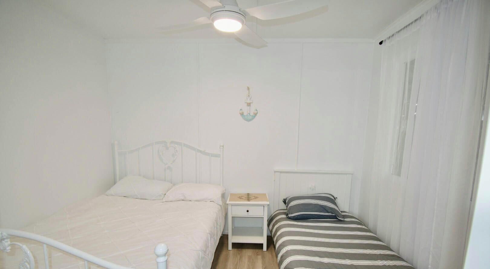 Een slaapkamer met een bed, nachtkastje, wandlamp en plafondventilator.