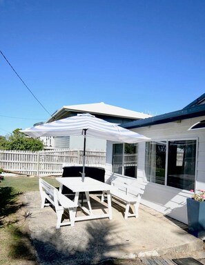 A patio with a white table and chairs, a covered seating area, and a house with large windows.