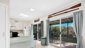 A modern kitchen with a glass counter, a refrigerator, and a dining area with a table and chairs. - Spacious Open Plan Villa with Complex Pool (Woodgate)