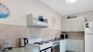 A compact kitchen with a stove, microwave, and dishwasher, white cabinets, and a small shelf with decorative bottles. - Spacious Open Plan Villa with Complex Pool (Woodgate)