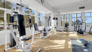 A gym with various exercise machines, large windows, and a wooden floor. - Lovers Key Resort 1201 (Fort Myers Beach)