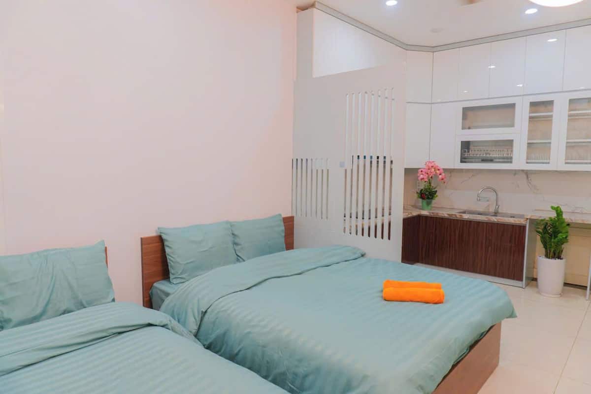 A bedroom with two beds, a small kitchenette, and a bathroom with a shower.
