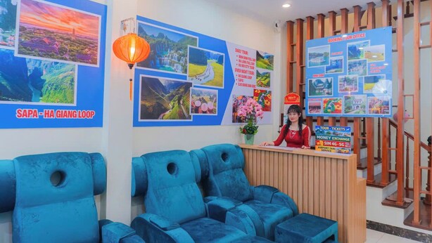 Un'area della reception di un hotel con una scrivania in legno, sedie blu e una parete che espone diverse foto di viaggio e informazioni.