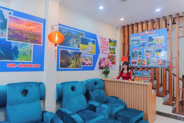 Zona de recepción de hotel con un mostrador de madera, sillas azules y una pared que exhibe diversas fotografías y datos de viaje.
