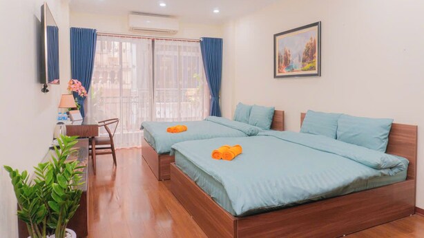 A hotel room with two beds, a desk, a chair, a potted plant, and a painting on the wall. - Dream Comes True (Hanoi)