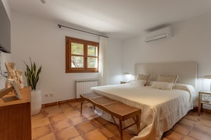 A bedroom with a bed, a bedside table, a lamp, a window, a radiator, and a potted plant.