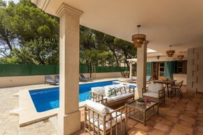 A poolside area with a rectangular pool, wicker furniture, and a view of trees.