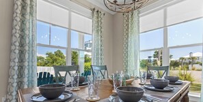Une table à manger dressée pour quatre personnes, avec des bols et des verres foncés, posée sur une table en bois, offrant une vue sur l’extérieur grâce à de grandes fenêtres.