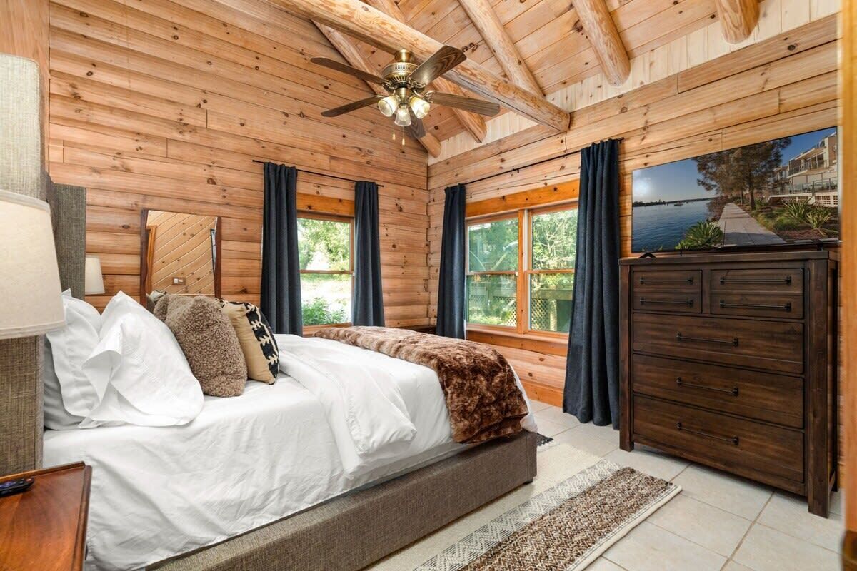 A wooden-paneled bedroom with a bed, a dresser, and a television.