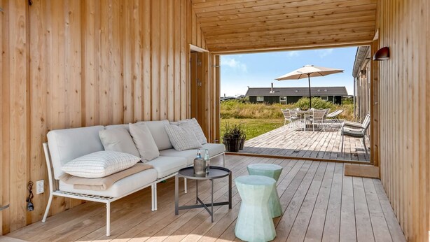 A wooden deck with a white sofa, a small round table, and two stools.