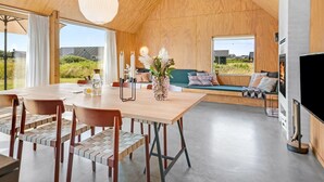 A modern interior with a wooden ceiling, a dining area with a table and chairs, a sofa with cushions, and a fireplace.