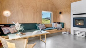 A modern interior with a wooden ceiling, a green sofa, a white table, and a fireplace.