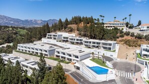A modern hotel complex with multiple buildings, a swimming pool, and a view of the surrounding landscape.