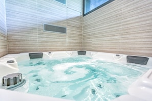 A hot tub with a view of the sky through a window, surrounded by tiled walls.
