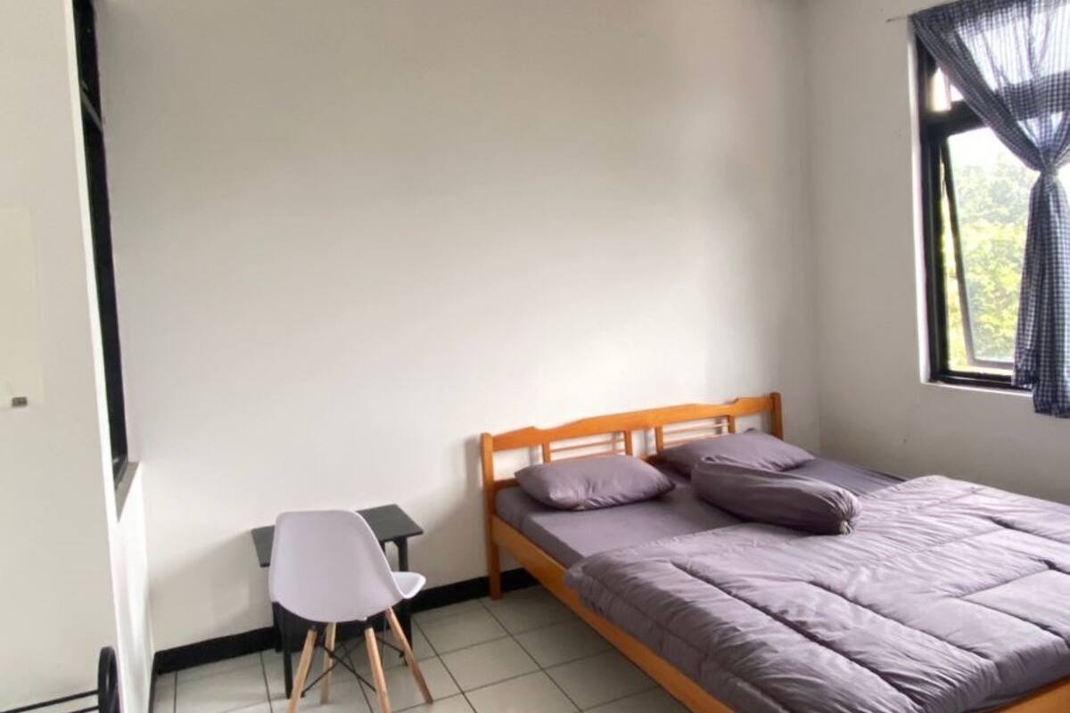 A bedroom with a bed, a chair, a window with curtains, and a tiled floor.