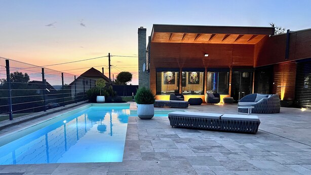 Un área de piscina exterior moderna con una piscina rectangular, sillas de descanso y una zona de estar cubierta.