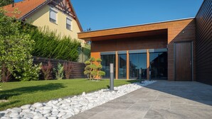 Un edificio moderno con fachada de madera, ventanas amplias y un camino de piedra que conduce a la entrada.
