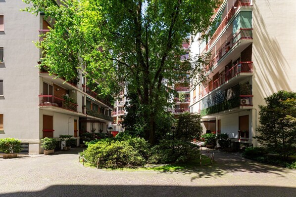 A courtyard with a central tree surrounded by buildings with balconies and potted plants.