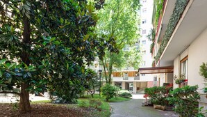 A courtyard with a tree, potted plants, a pathway, and a building with balconies. - GuestHost - Beautiful 35 sqm apartment located on the mezzanine floor of a building WITHOUT elevator (stairs to access it). The property is located 11 minutes by public transport from City Life, the largest pedestrian area in Milan, and from MiCo, the la (Milano)