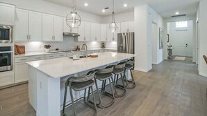A modern kitchen with white cabinets, stainless steel appliances, and a large island with bar stools.