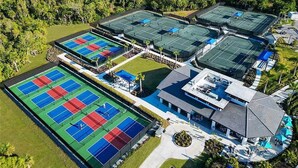 An aerial view of a resort with multiple tennis courts, a swimming pool, and a large landscaped area.
