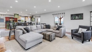 Amplia sala de estar con un sofá seccional gris, un sillón negro y una mesa de comedor con sillas.
