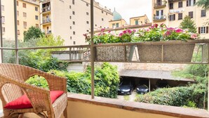 Een balkon met rieten meubels, uitzicht op een stadsgezicht en een auto die eronder geparkeerd staat.