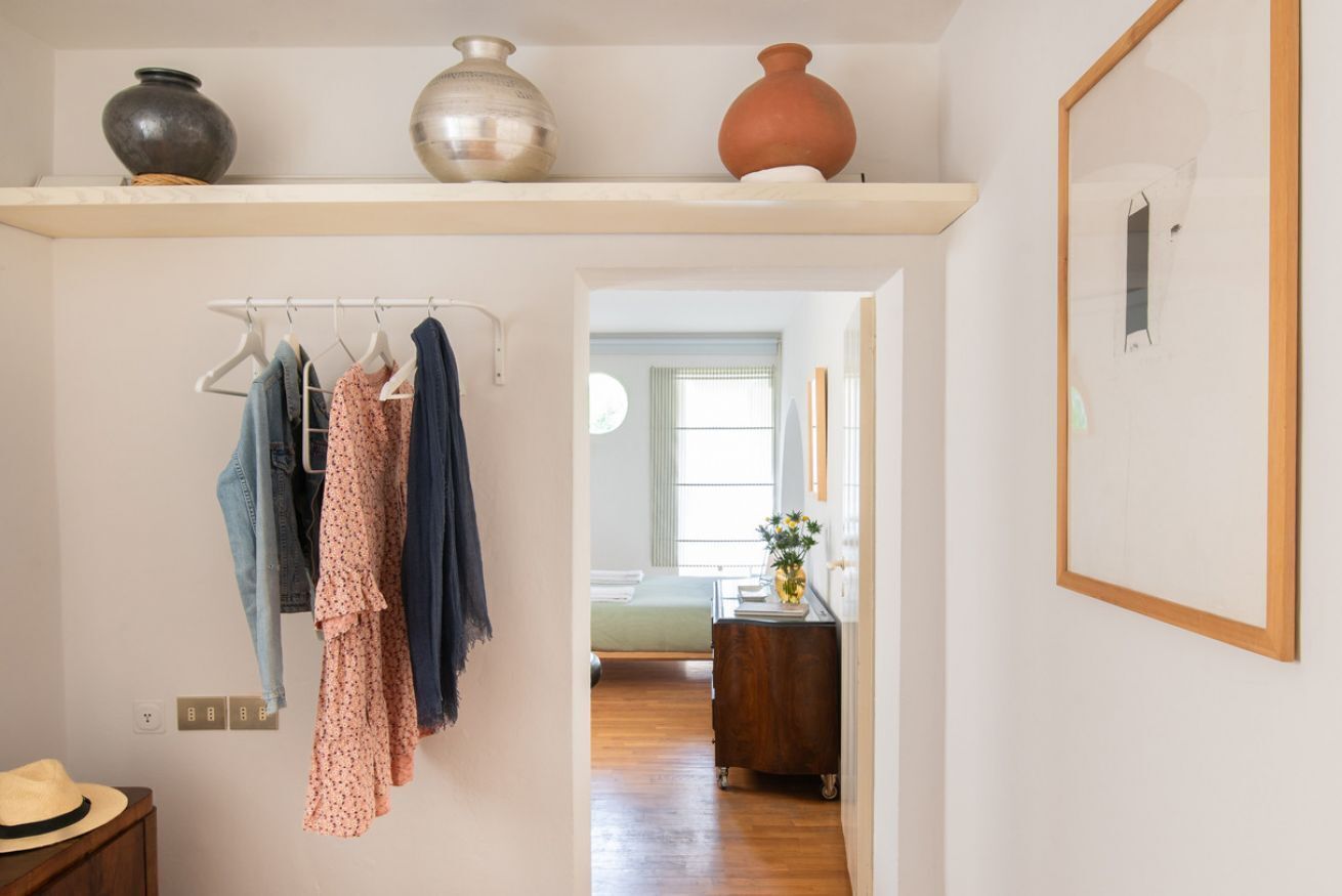 A hallway with a clothing rack, a hat on a table, and a wooden dresser.