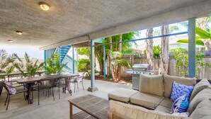 Un patio al aire libre con una mesa de comedor, sillas, un sofá y una zona de barbacoa.