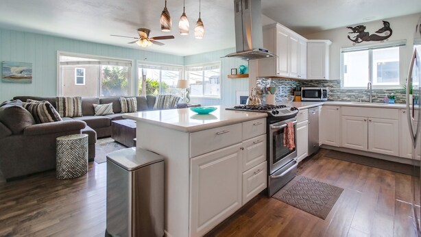 Una cocina moderna con armarios blancos, una isla central y un comedor con sofá.
