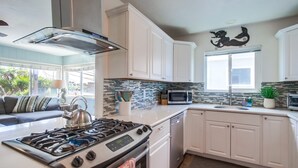 Cocina moderna con armarios blancos, estufa a gas, microondas y ventana con vistas a zonas verdes.