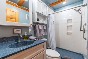 A bathroom with a sink, toilet, shower, and cabinets. - Pine Cabin- Log cabin close to Custer (Custer)